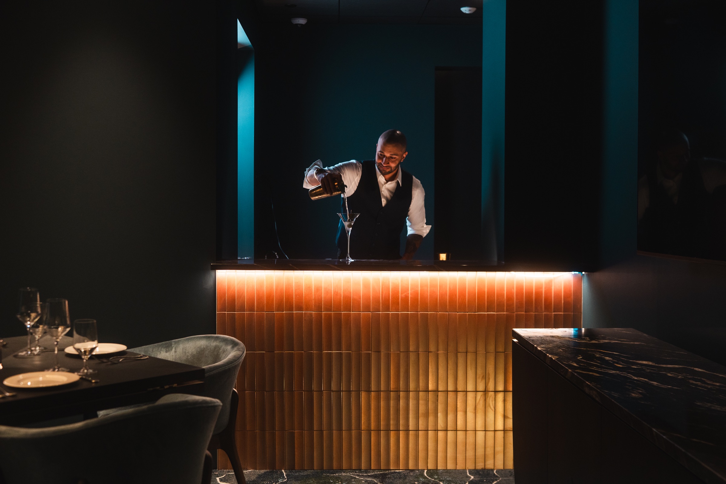 Bartender pouring a cocktail behind an illuminated bar