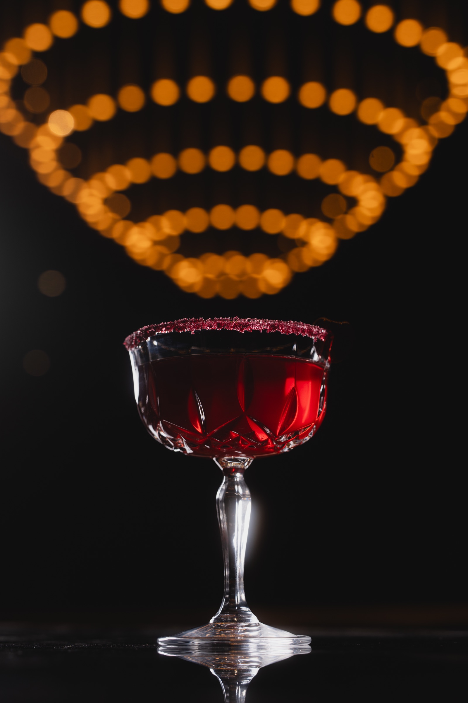 Deep red cocktail beneath warm circular lights in a dark lounge